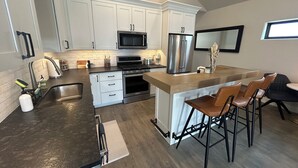 A modern kitchen with white cabinets, stainless steel appliances, and a bar area with stools.