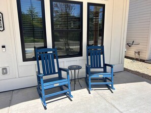 Dos sillas Adirondack azules frente a una casa con ventanas amplias y una pequeña mesa entre ellas.