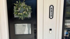 A black front door with a wreath, a mailbox, and a house number sign.