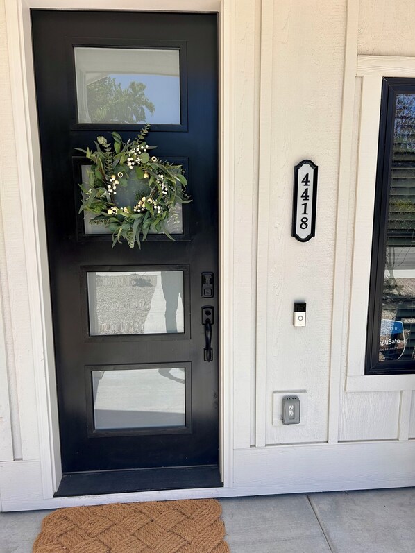 A black front door with a wreath, a mailbox, and a house number sign.
