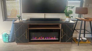 A modern entertainment unit with a flat-screen TV, a fireplace, and a potted plant.