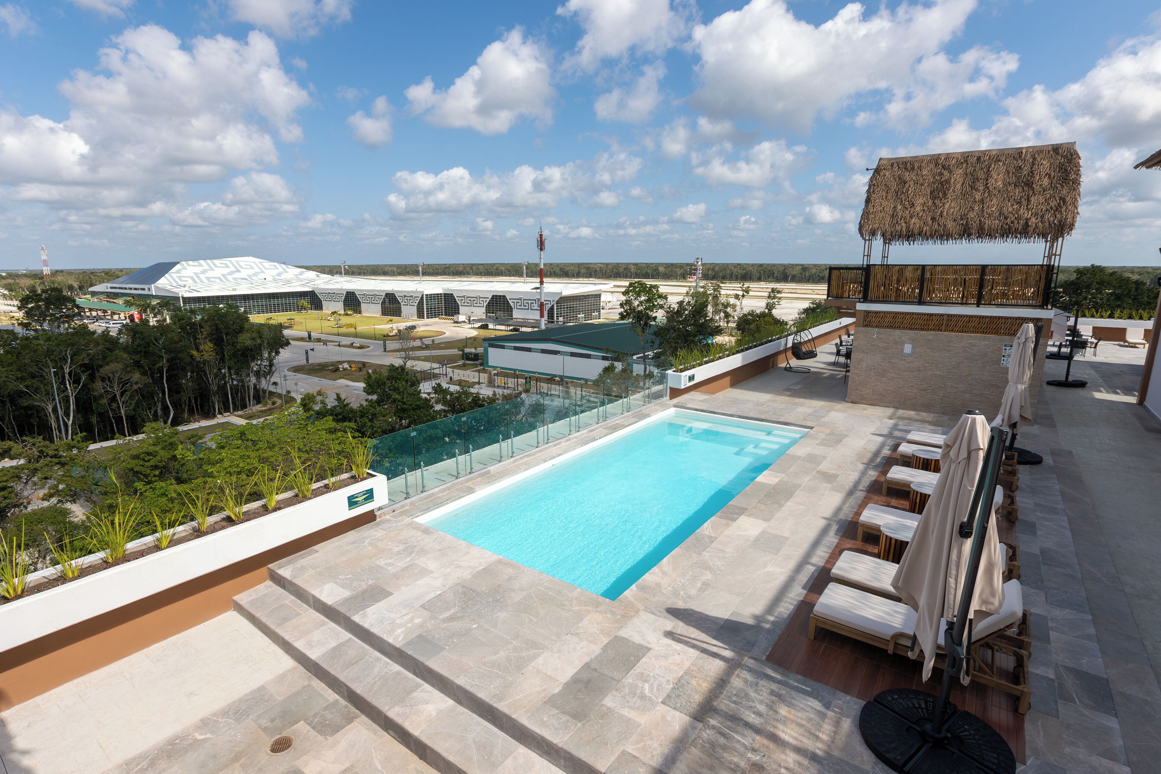 Zona de piscina en la azotea con vistas despejadas del paisaje circundante, incluyendo un edificio grande y árboles.