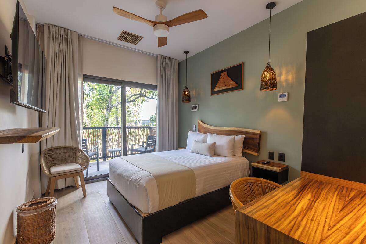 Ein Hotelzimmer mit Bett, einem Holztisch, einem Stuhl, einem Deckenventilator und einem Balkon mit Gartenmöbeln.