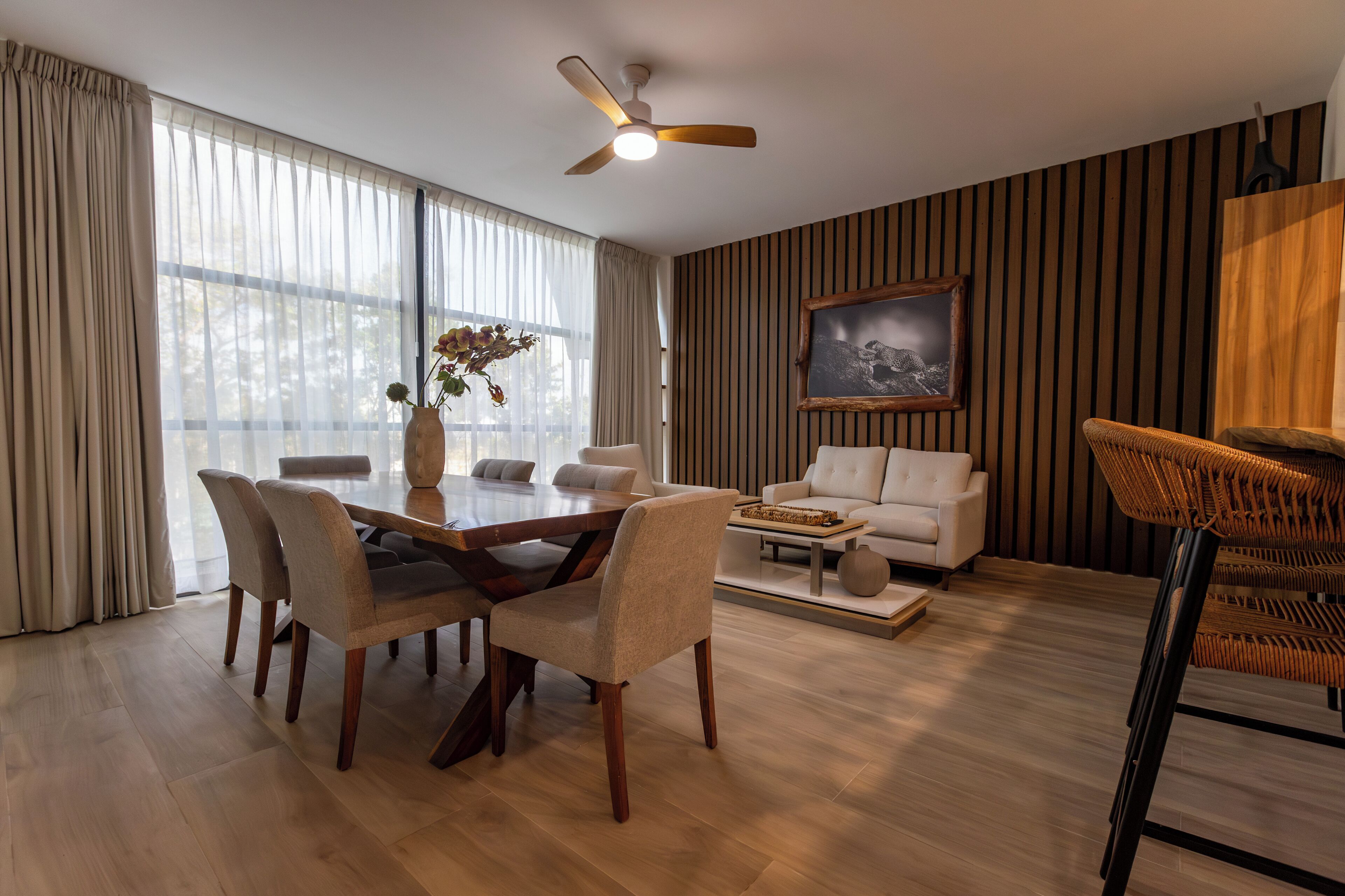 A modern living room with a dining area, a white sofa, a wicker chair, and a ceiling fan.