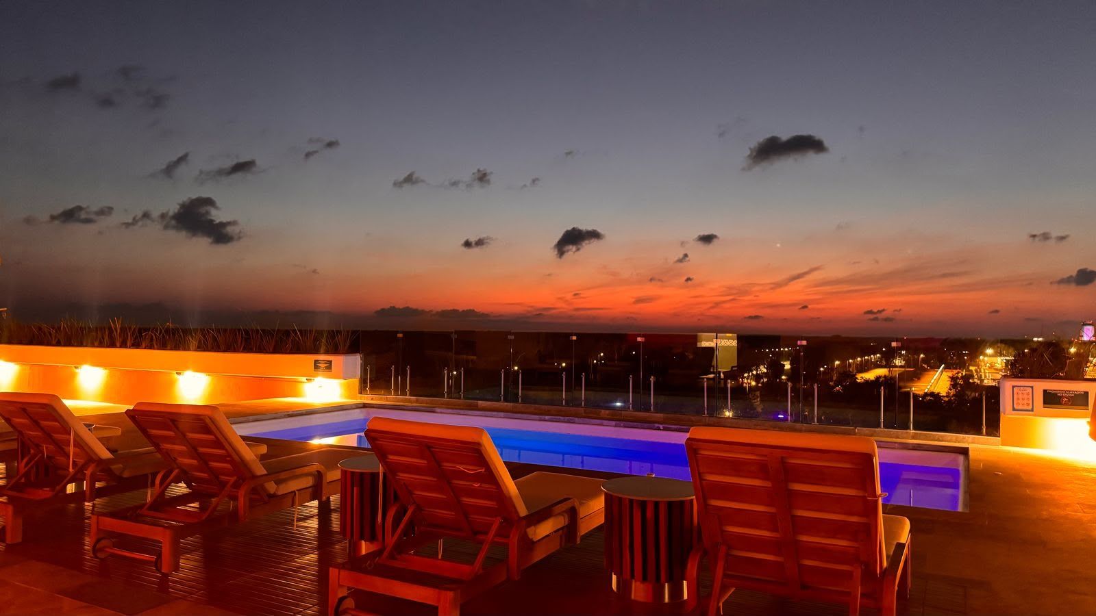 Zona de piscina en la azotea con sillones de descanso y vistas al horizonte de la ciudad al anochecer.