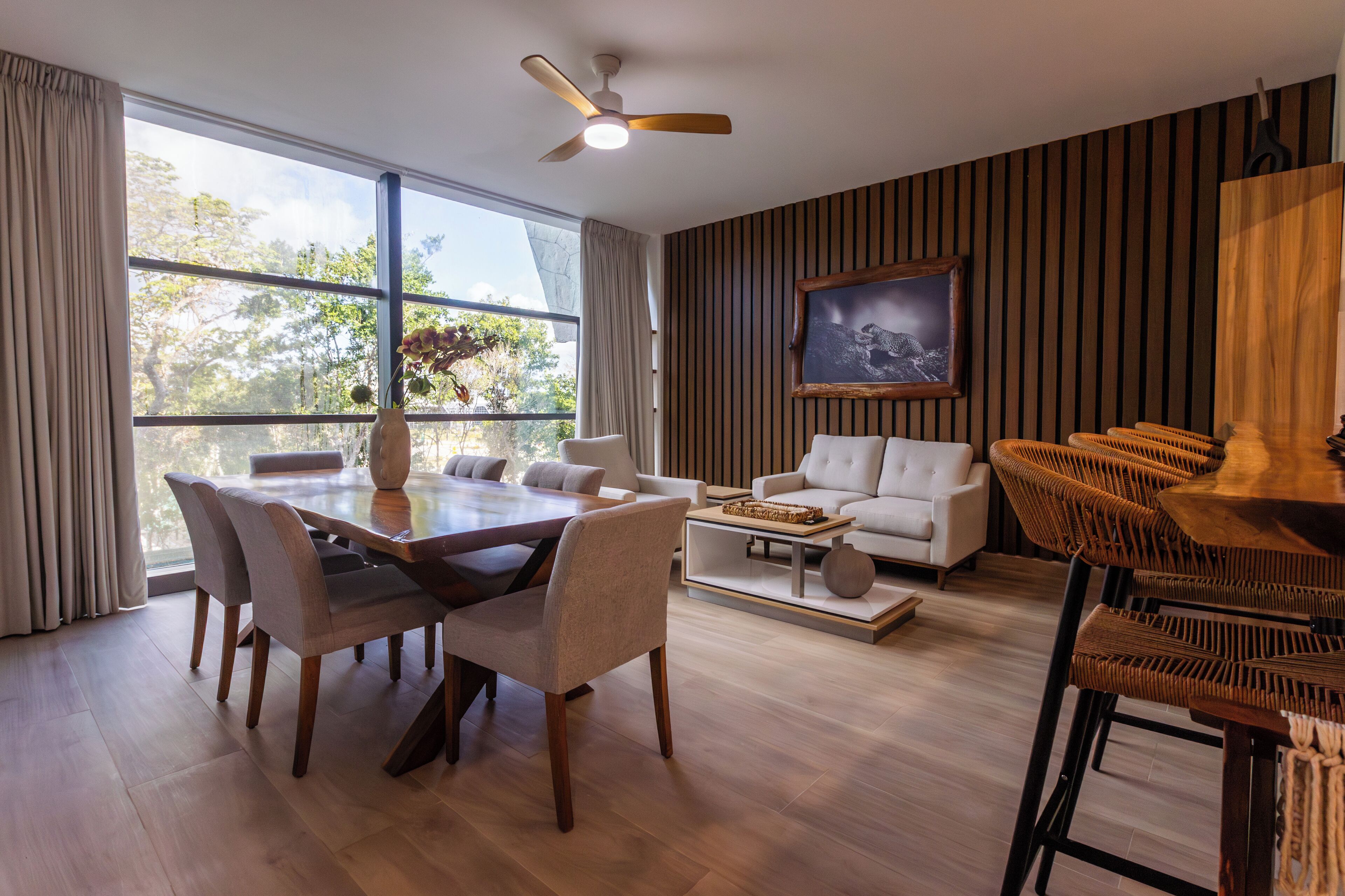 Un salon moderne avec un coin repas, de grandes fenêtres et un ventilateur de plafond.