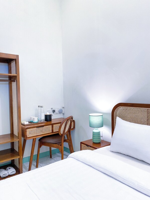 Une chambre d’hôtel avec un lit, un bureau avec une chaise, une lampe et une étagère où sont rangées des chaussures.