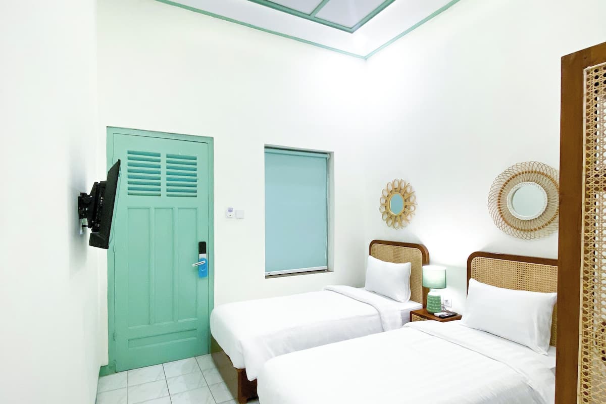 A room with two beds, a door, a window, and a ceiling light fixture.
