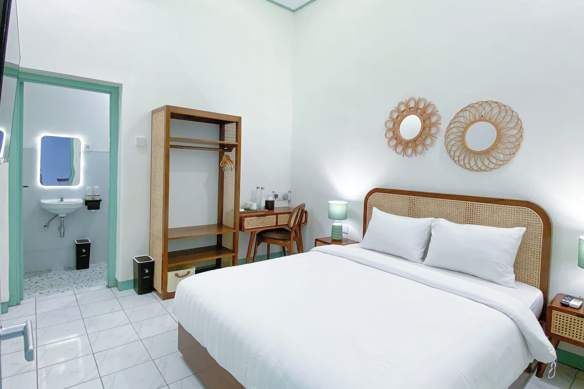 A hotel room with a bed, a desk, a chair, a mirror, a sink, and two wall decorations.