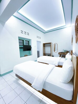 Une chambre d’hôtel moderne avec deux lits, un grand miroir, un petit bureau et un téléviseur fixé au mur.