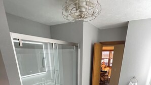 A modern bathroom with a glass shower enclosure, a white sink, and a small trash bin.