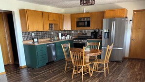 A kitchen with wooden cabinets, a dining table with chairs, a refrigerator, and a ceiling fan.
