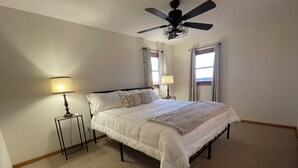 A bedroom with a bed, two bedside tables, a ceiling fan, and two windows with curtains.