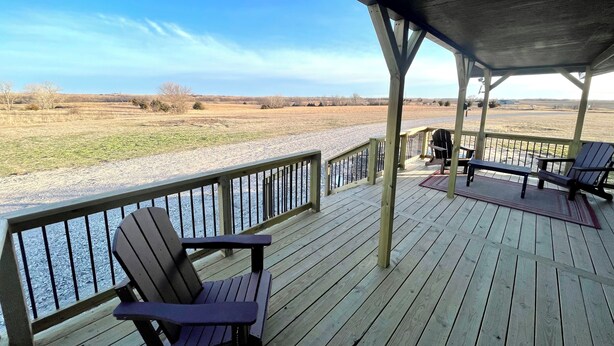 A wooden deck with Adirondack chairs overlooking a gravel path and open fields.