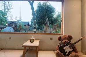 Et værelse med et stort vindue, et lille bord og en bamse som spiller guitar.