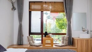 A bedroom with a bed, a wooden bench, two chairs, a window with a view, and a bathroom with a sink and mirror. - Leisurely residence (Jinyun)