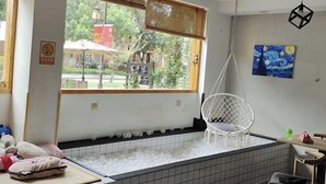 A room with a large window, a hanging chair, and a view of a street with a red building. - Leisurely residence (Jinyun)