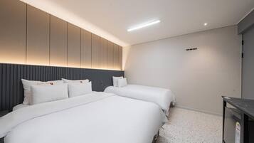 A modern hotel room with two beds, a dark headboard, a small desk, and a ceiling light.