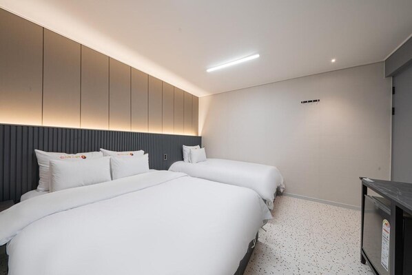 A modern hotel room with two beds, a dark headboard, a small desk, and a ceiling light. - EG STAY hotel (Gwangju)