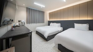 Hotellihuone, jossa on kaksi sänkyä, työpöytä tuolilla, taulutelevisio ja suuri ikkuna, jossa on verhot.