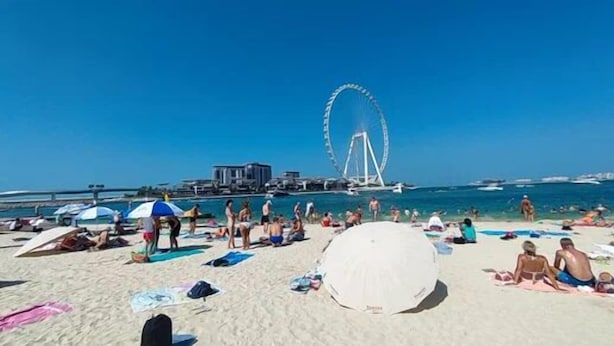 A beach with people sunbathing, umbrellas, and a large Ferris wheel in the background. - Large 5br, Sea & JBR view, Easy Beach Access, Family Friendly! (Dubai)
