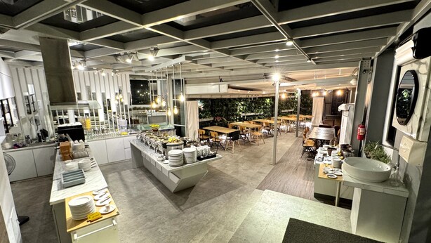 A modern restaurant with a central island, multiple dining tables, and a green wall in the background. - Unisi Hotel Malioboro (Yogyakarta)