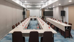 A conference room with a long table, chairs, and a projector screen. - Unisi Hotel Malioboro (Yogyakarta)
