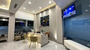 A modern hotel reception area with a marble reception desk, comfortable seating, a large digital screen displaying content, and a view of the outside through large windows. - Unisi Hotel Malioboro (Yogyakarta)