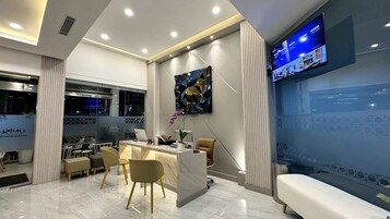 A modern hotel reception area with a marble reception desk, comfortable seating, a large digital screen displaying content, and a view of the outside through large windows.