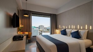 A modern hotel room with a large bed, a desk with a flat-screen TV, and a city view through the window. - Unisi Hotel Malioboro (Yogyakarta)