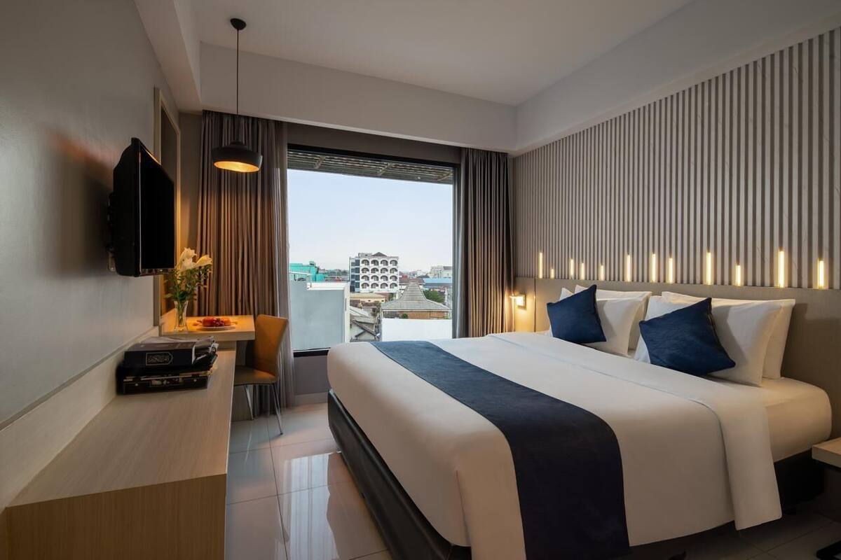 Ein modernes Hotelzimmer mit einem großen Bett, einem Schreibtisch mit Flachbildfernseher und Blick auf die Stadt durch das Fenster.