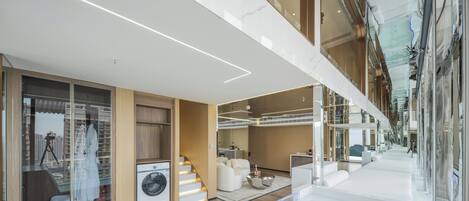 A modern hotel interior with a spacious lobby, a visible staircase, and a seating area with a coffee table.