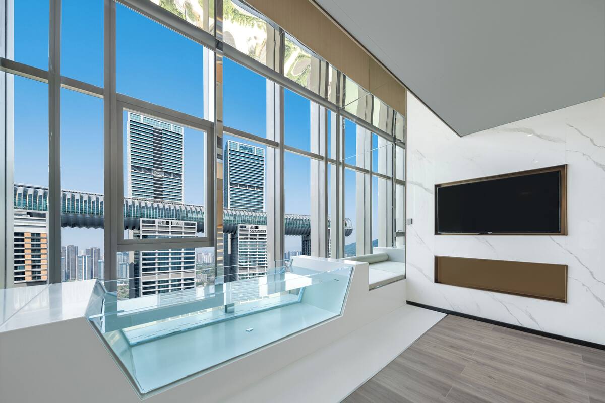 A modern interior with large windows, a glass railing, a mounted TV, and a city view.