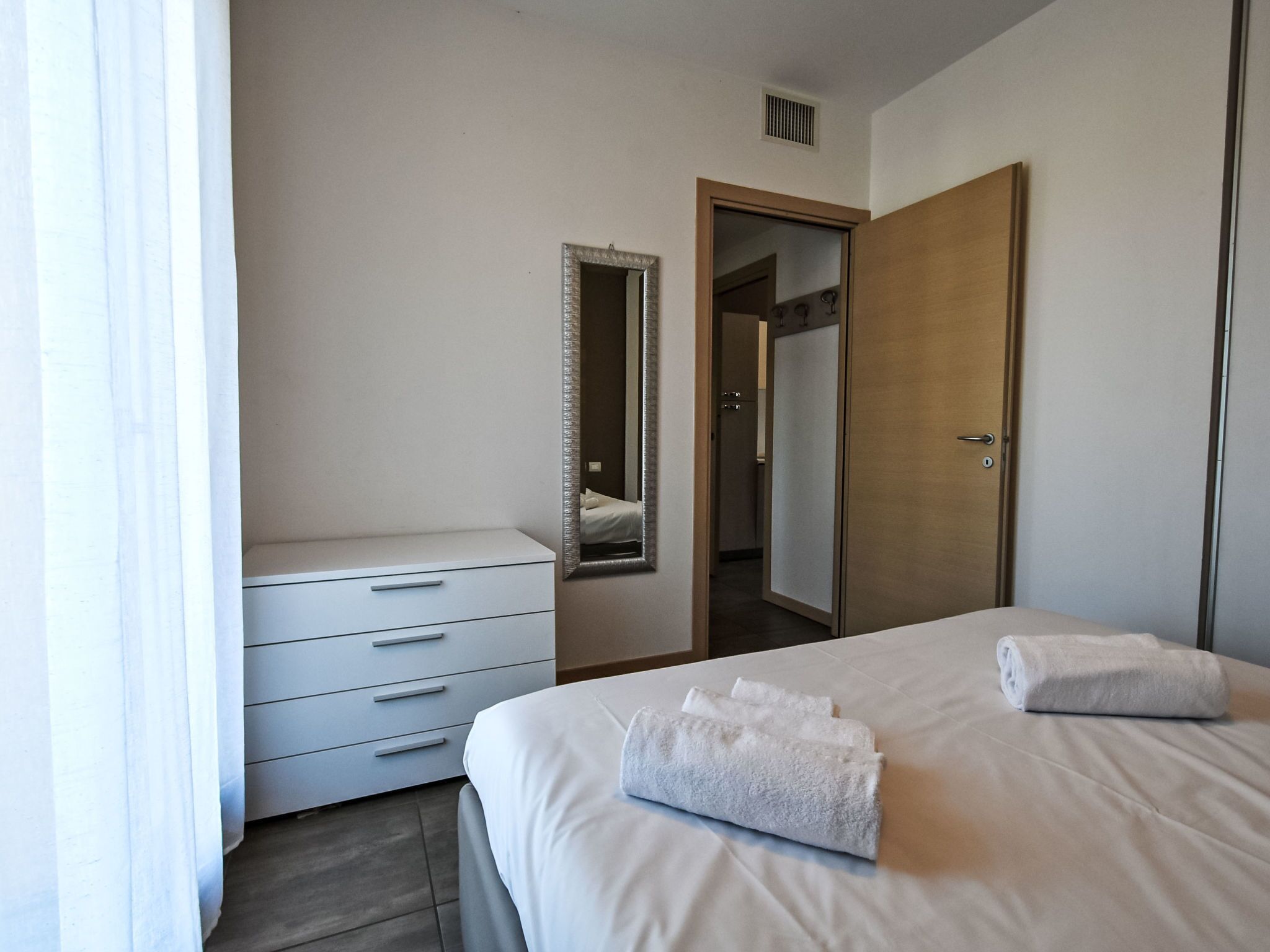 Quarto de hotel com uma cama, penteadeira, espelho e porta.