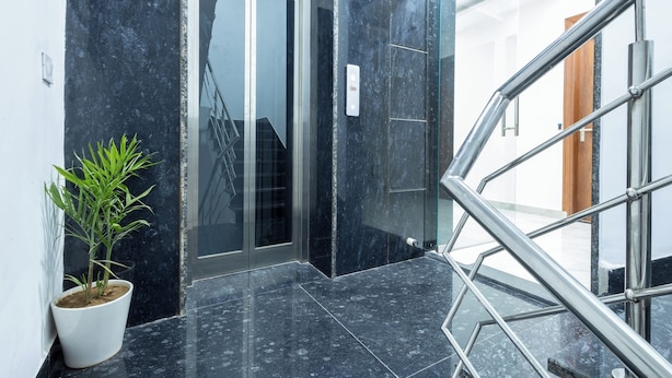 En moderne elevatorindgang med en potteplante, en glasdør og et metalgelænder.