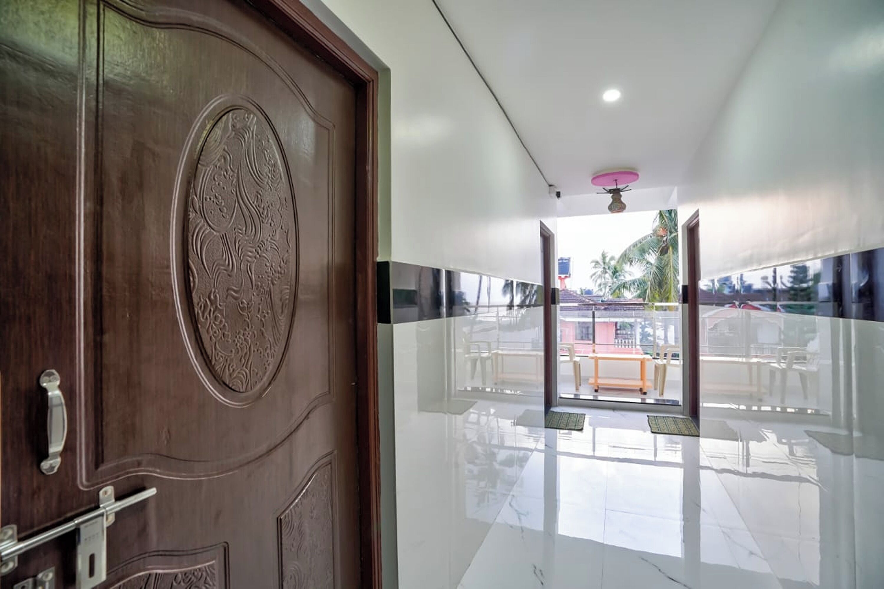 A hotel entrance with a wooden door featuring intricate carvings, a shiny tiled floor, and a view of the outside area including a table and chairs.