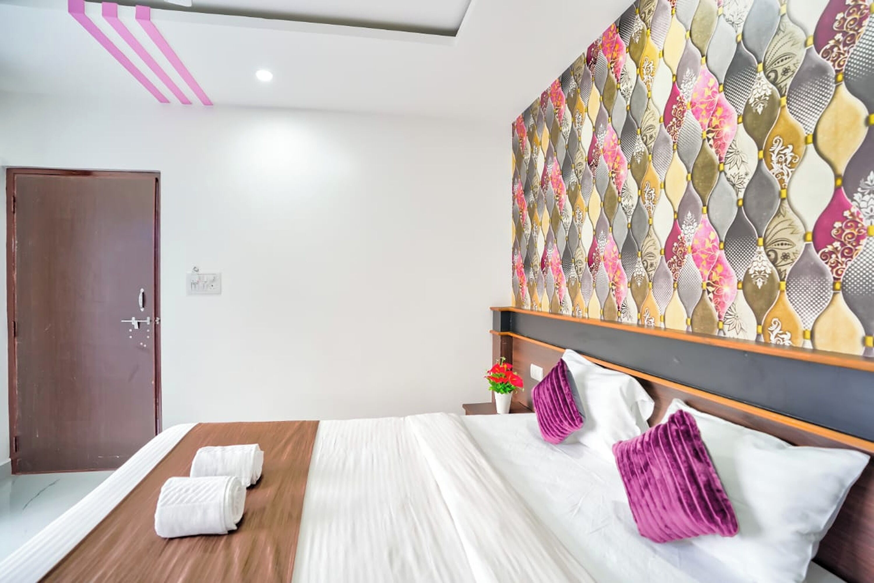 Una camera d'albergo con un letto, una testiera in legno, un pannello decorativo e una porta.