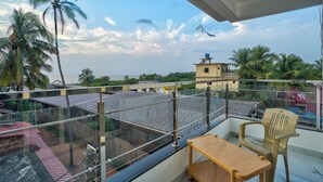 Ein Balkon mit Glasgeländer, einem Holztisch und einem Plastikstuhl.