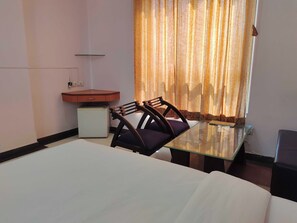 Ein Hotelzimmer mit einem Bett, einem kleinen Schreibtisch mit Stuhl, einem Kühlschrank und einem Fenster mit Vorhängen.
