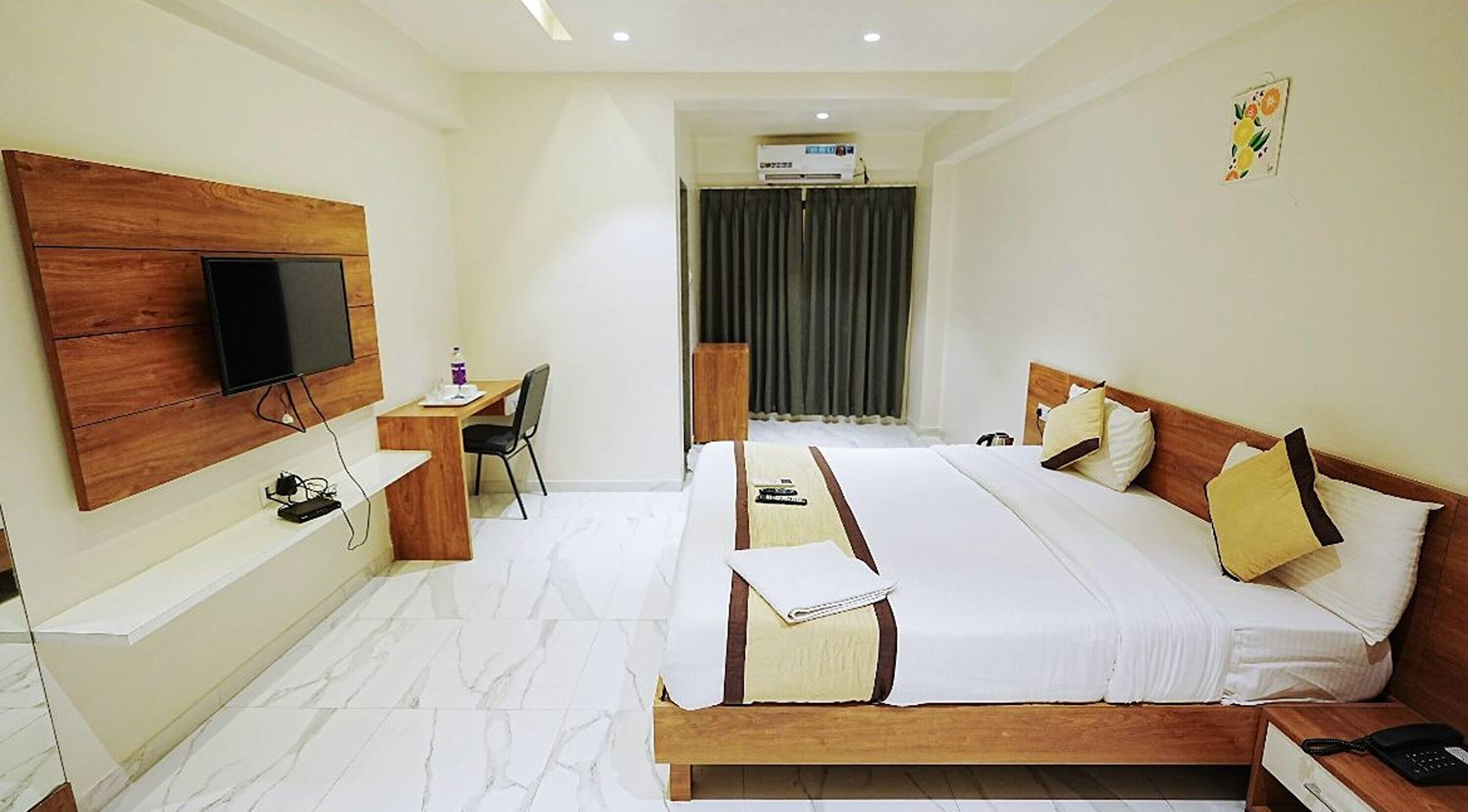 A hotel room with a large bed, a desk with a chair, a television mounted on the wall, and an air conditioning unit.
