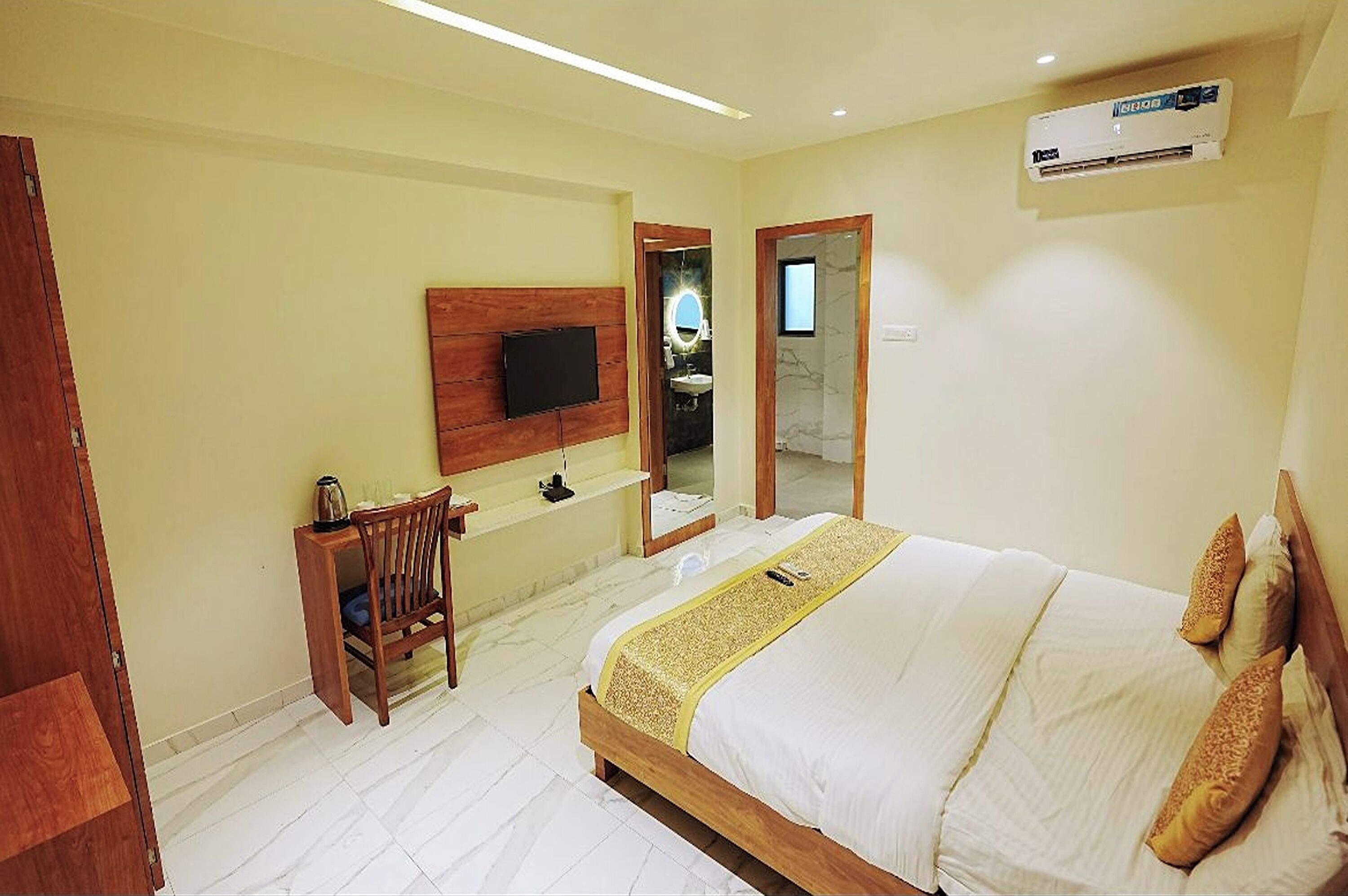 A hotel room with a bed, a desk, a TV mounted on the wall, and an air conditioning unit.