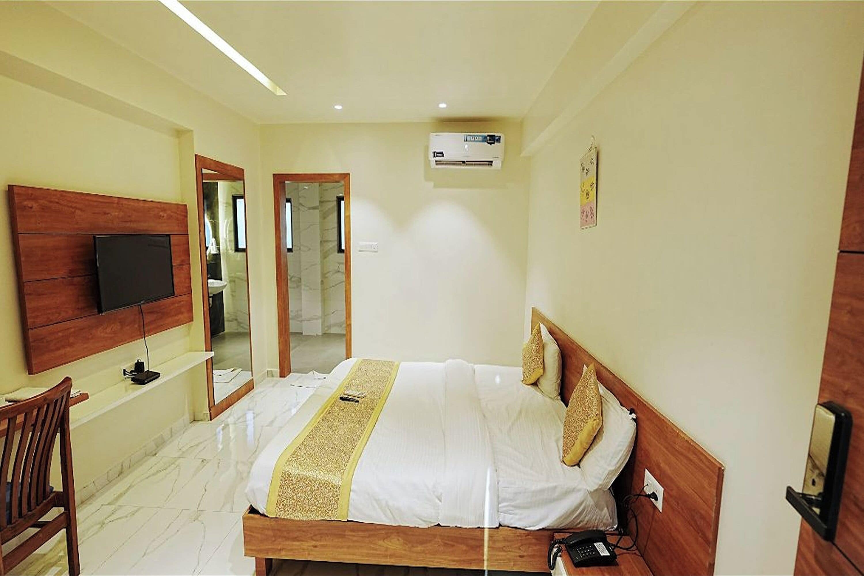 A hotel room with a bed, a TV mounted on the wall, a desk, and a chair.
