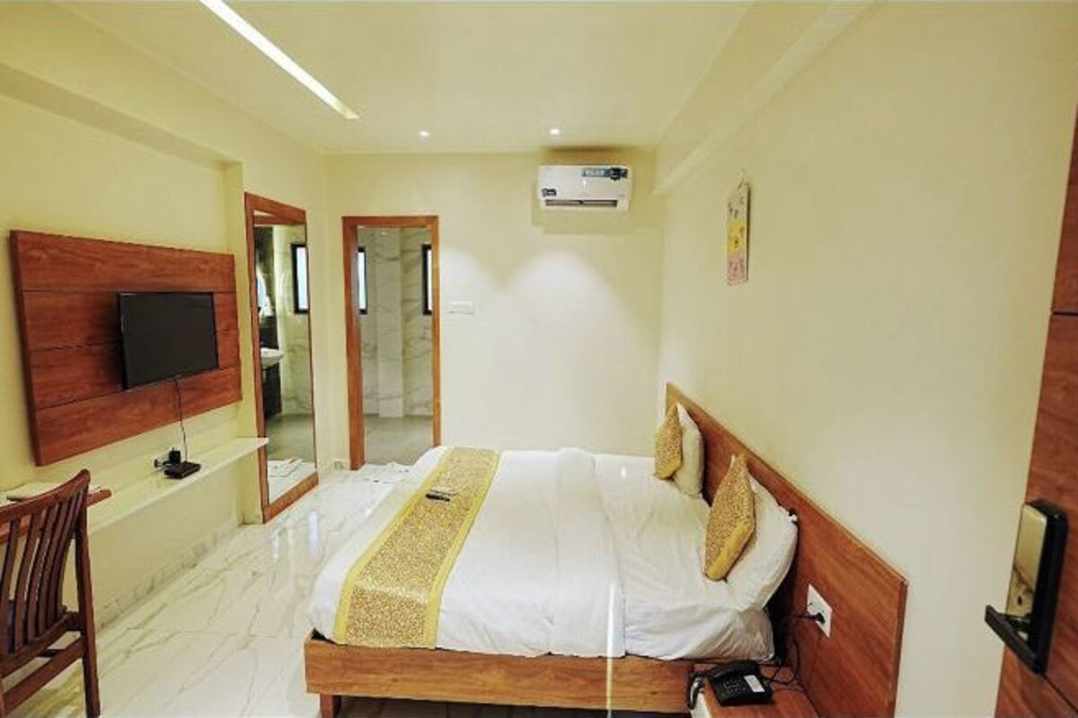 A hotel room with a bed, a TV mounted on the wall, a mirror, and a wooden chair.