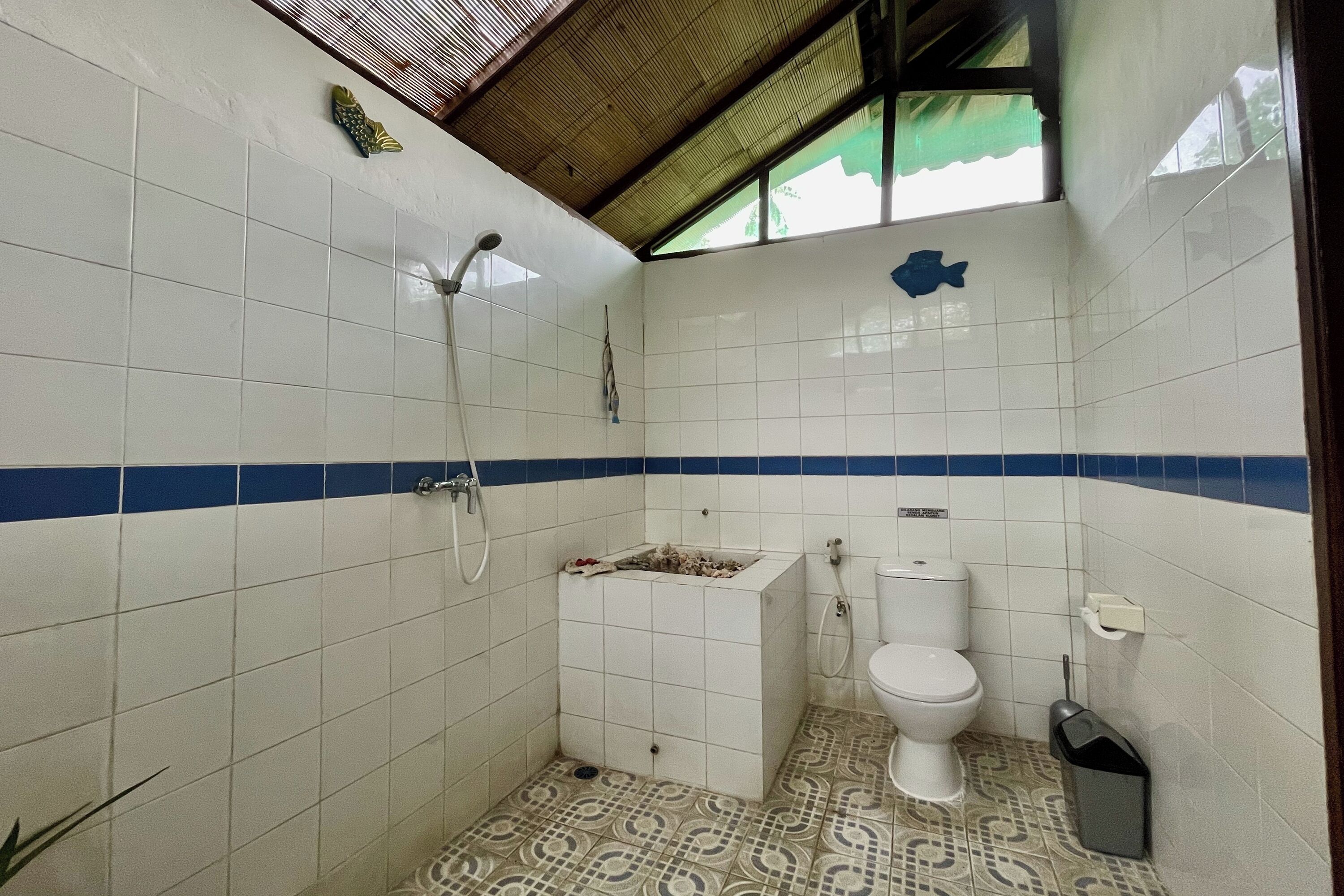 A bathroom with white tiled walls, a blue stripe, a shower, a toilet, and a patterned floor.