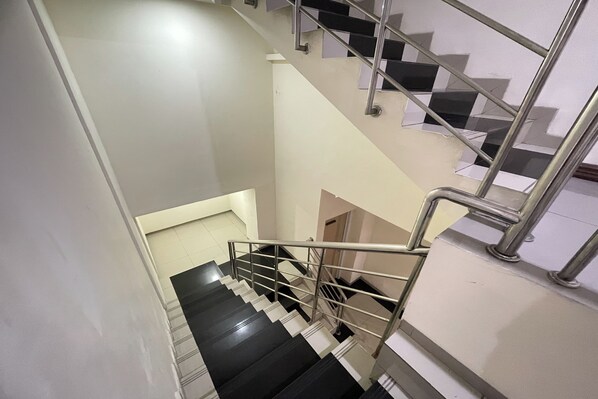 Una escalera con peldaños blancos y negros, barandillas de metal y una pared blanca.