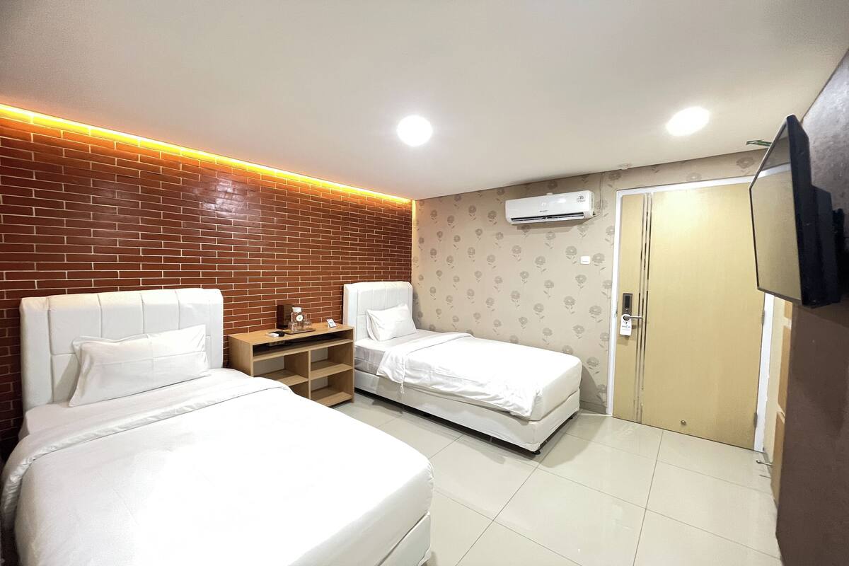 A hotel room with two beds, a brick accent wall, an air conditioning unit, and a wardrobe.