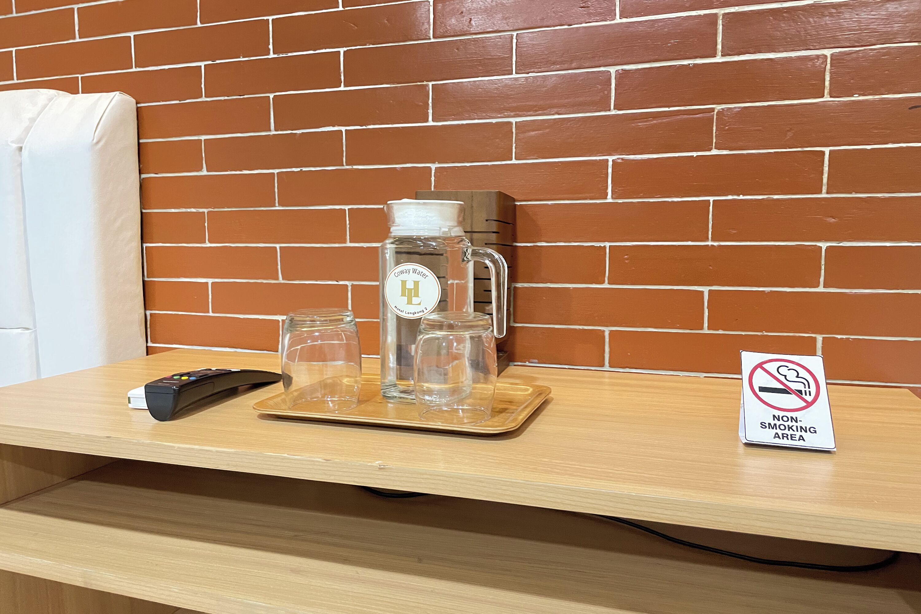 A wooden table with a coffee maker, glasses, and a remote control. A 'Non-Smoking Area' sign is visible.