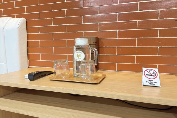 A wooden table with a coffee maker, glasses, and a remote control. A 'Non-Smoking Area' sign is visible. - Hotel Lengkong 2 (Bandung)