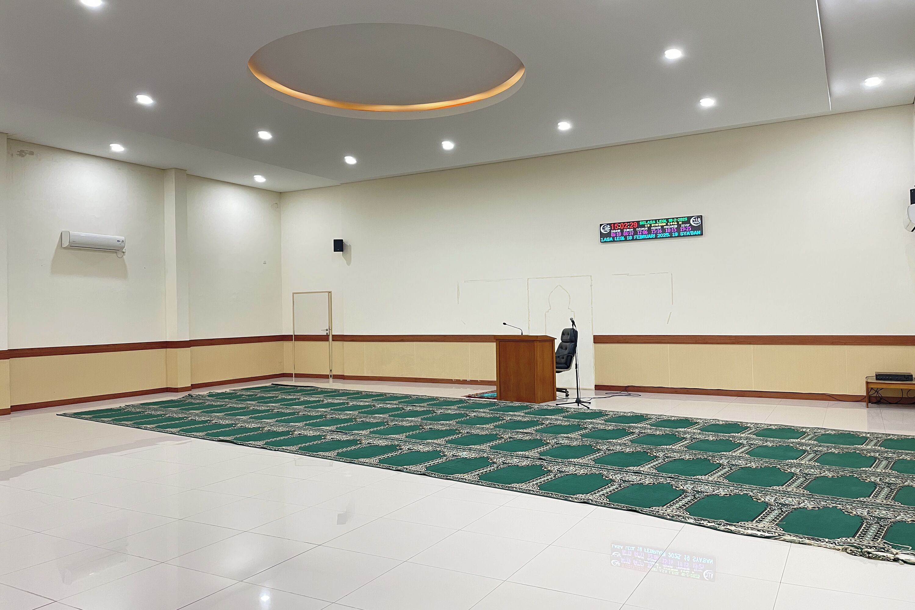 A spacious room with a green carpet, a podium, and a digital display on the wall.