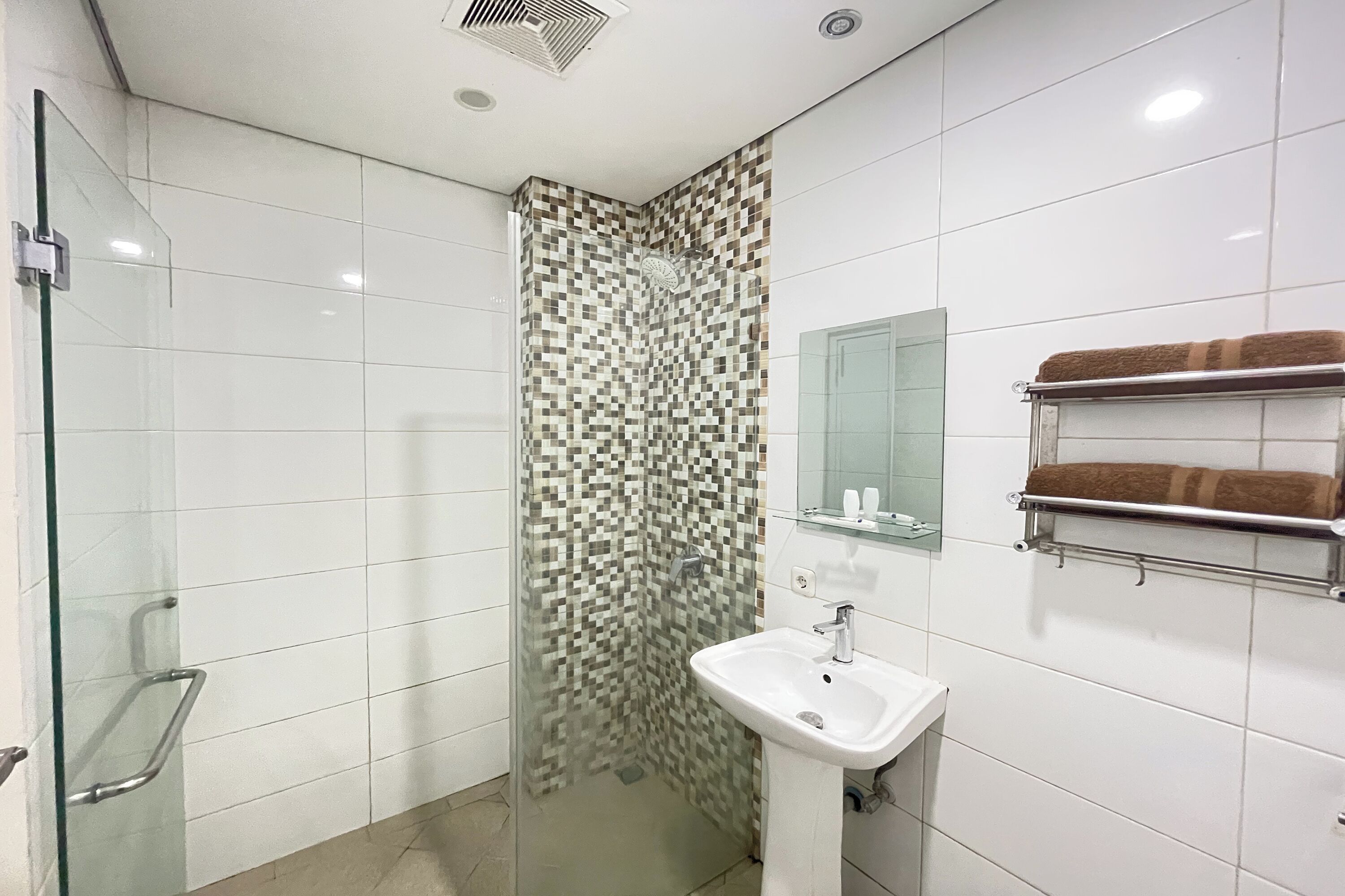 Een moderne badkamer met een douchecabine van glas, een witte wastafel en een handdoekrek met handdoeken.
